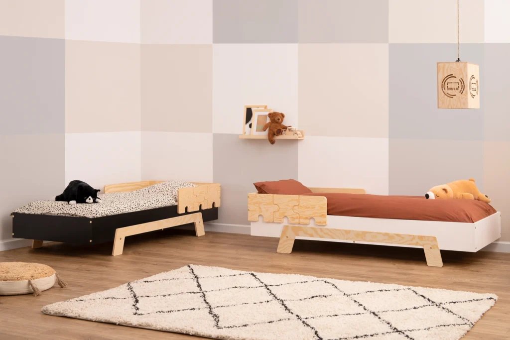 Deux lits en contreplaqué de pin avec des barrières en forme de puzzle dans une chambre lumineuse avec des peluches