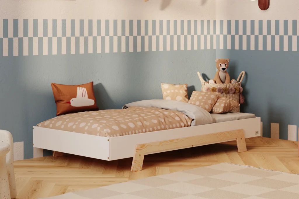 Lit enfant en contreplaqué de pin de couleur blanche, avec des pieds en bois naturel, placé dans une chambre d’enfant chaleureuse avec un mur bleu et beige et une literie aux tons chauds.