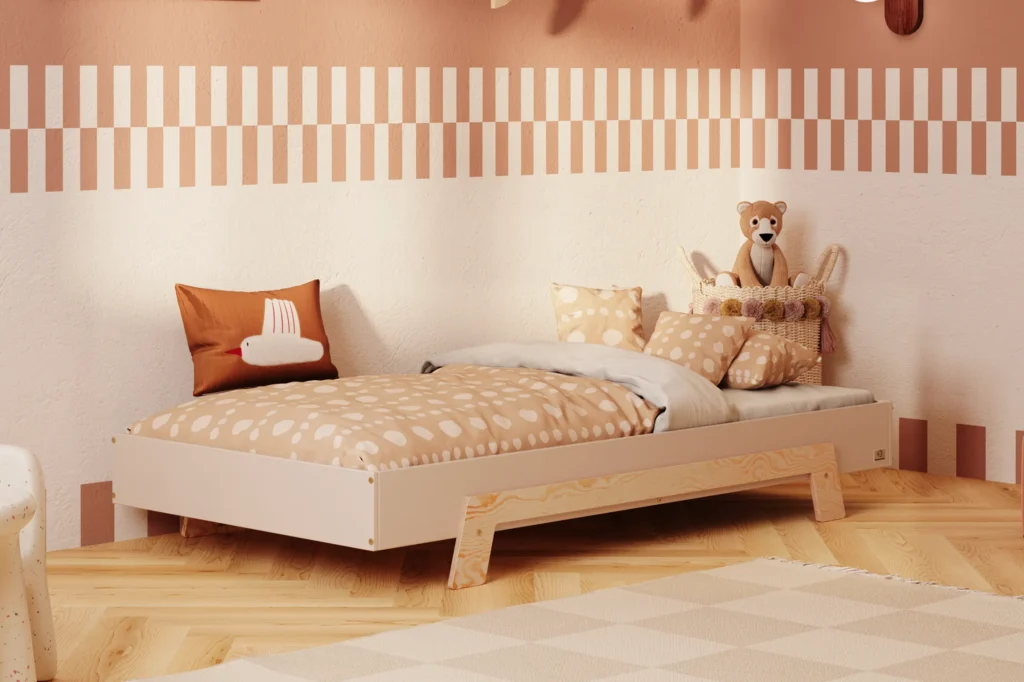 Lit enfant en contreplaqué de pin de couleur cachemire, avec des pieds en bois naturel, placé dans une chambre d’enfant chaleureuse avec un mur beige et une literie aux tons chauds.