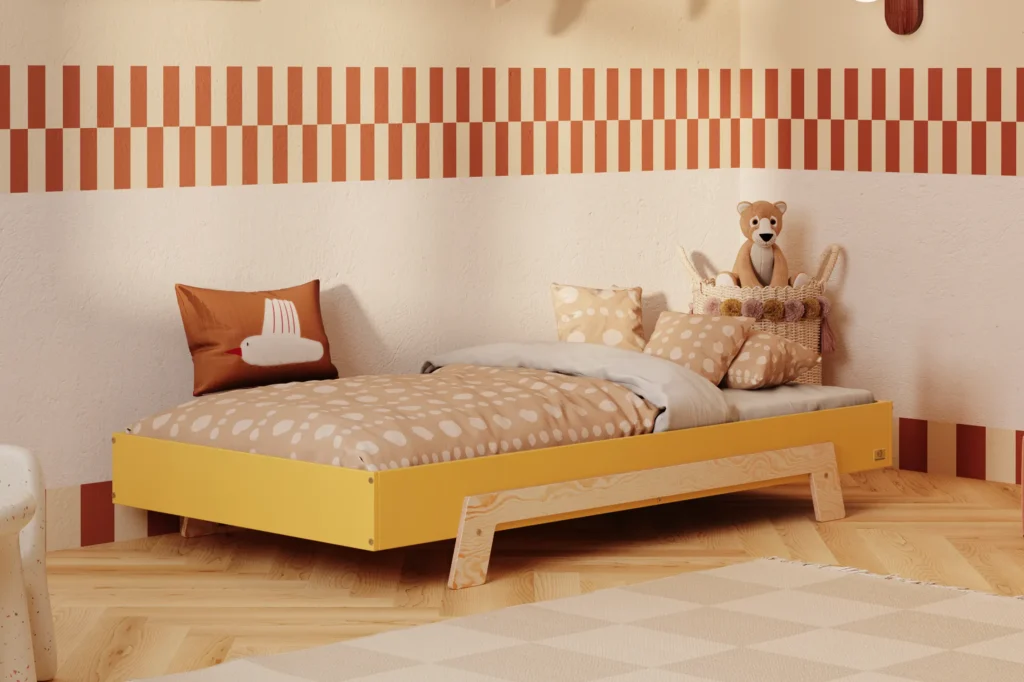 Lit enfant en contreplaqué de pin de couleur moutarde, avec des pieds en bois naturel, placé dans une chambre d’enfant chaleureuse avec un mur beige et une literie aux tons chauds.