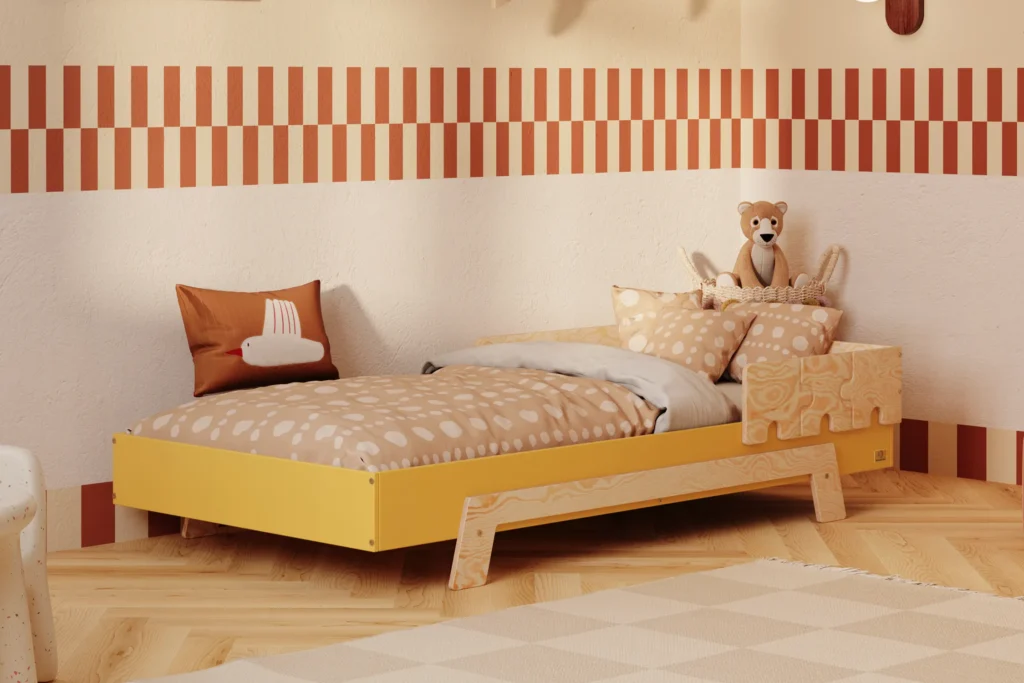 Lit enfant en contreplaqué de pin de couleur moutarde, avec une barrière en finition bois naturel et des pieds en bois naturel, placé dans une chambre d’enfant chaleureuse avec un mur beige et une literie aux tons chauds.