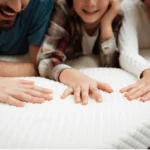 Une famille allongée sur le matelas teste sa douceur en touchant la surface avec la main