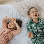 Deux enfants sur un lit avec draps blancs, moment de complicité