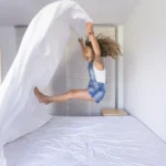 Petite fille jouant sur un lit avec du linge de lit blanc