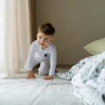 Jeune enfant en pyjama sur un lit, près de la fenêtre